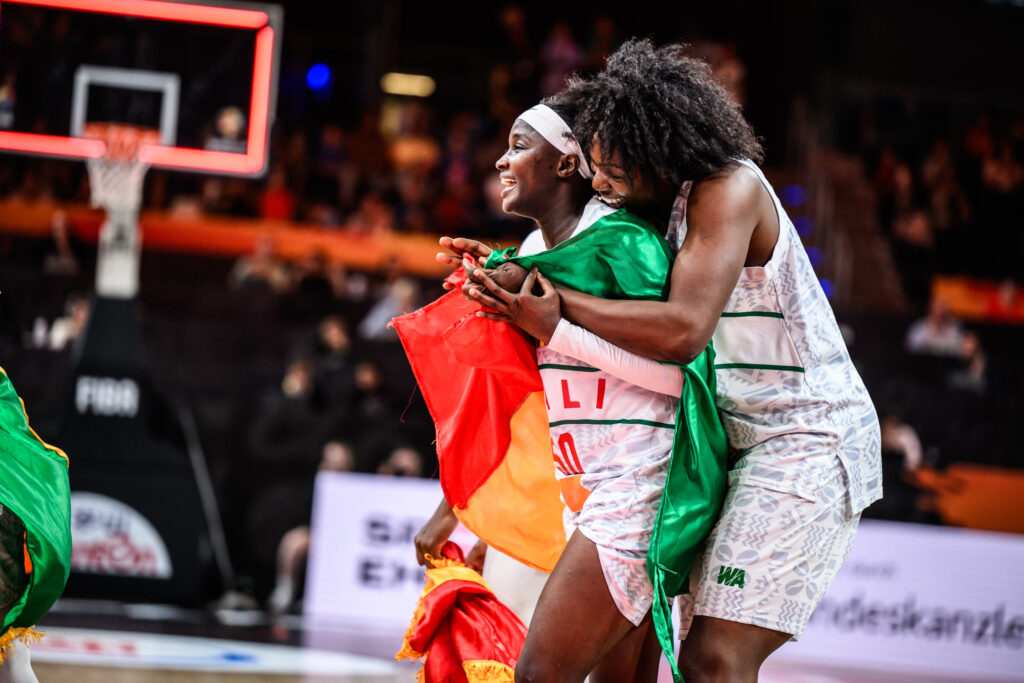 Deux joueuses maliennes s'enlacent, drapeau du Mali sur les épaules, après la victoire face à l'Espagne